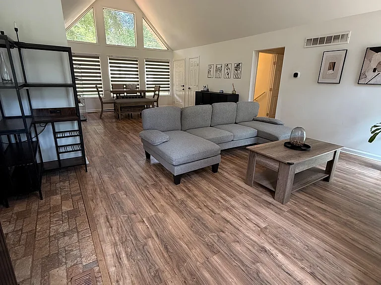 Open-concept living area with vaulted ceilings, large picture windows, and flexible space for seating and a dining set.
