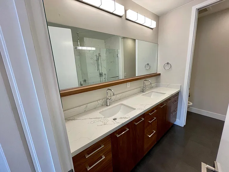 Primary bath with 9 drawers, seperate toilet room with door on the right, cool wood shelf below mirror