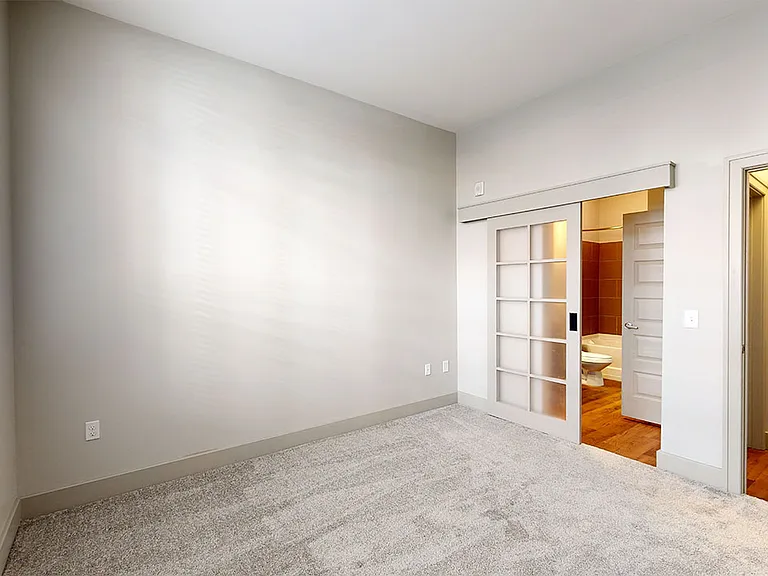 Spacious apartment bedroom with attached bathroom and wood-style flooring.