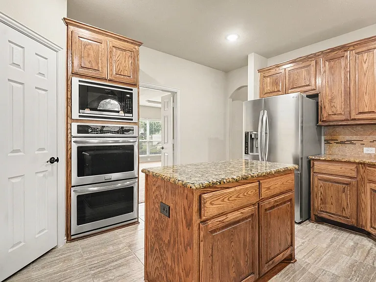Kitchen featuring wood cabinetry, stainless steel appliances, a center island with a speckled countertop, and tiled flooring