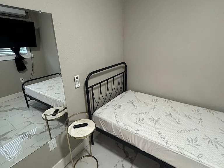 Private bedroom with a bed frame, side tables, wall-mounted TV, and tile flooring for easy maintenance.