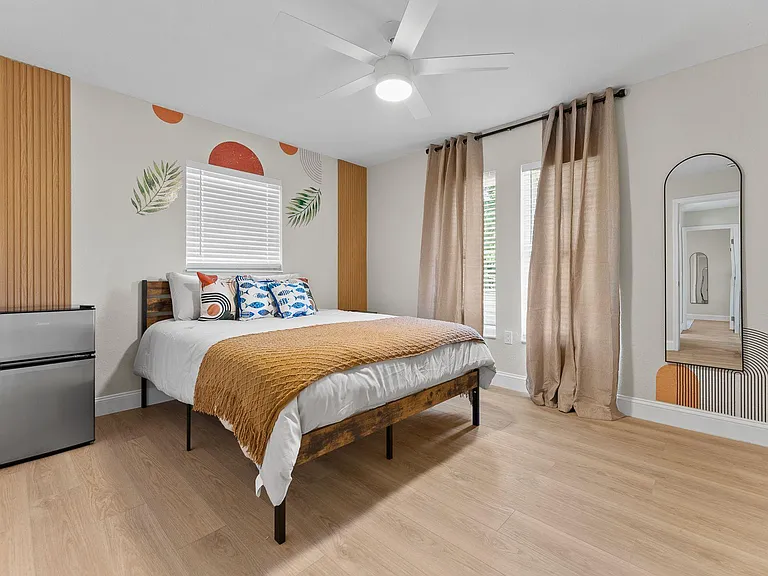 Furnished bedroom with ceiling fan, large windows with coverings, and in-room mini fridge for added convenience.