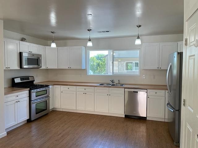 Large, open kitchen with stainless steel appliances including fridge with bottom freezer, dishwasher, microwave and double range oven. Butcher block counters and ample storage.