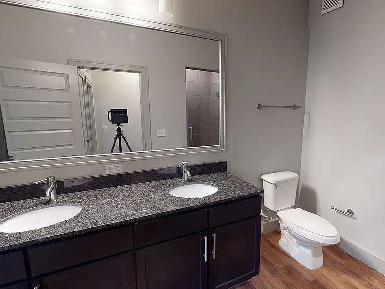 Apartment bathroom with glass enclosed shower, wood-style flooring and double sinks.