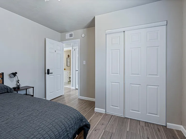 Private bedroom with wood-look flooring, a bedside table, and a spacious sliding-door closet for easy storage.