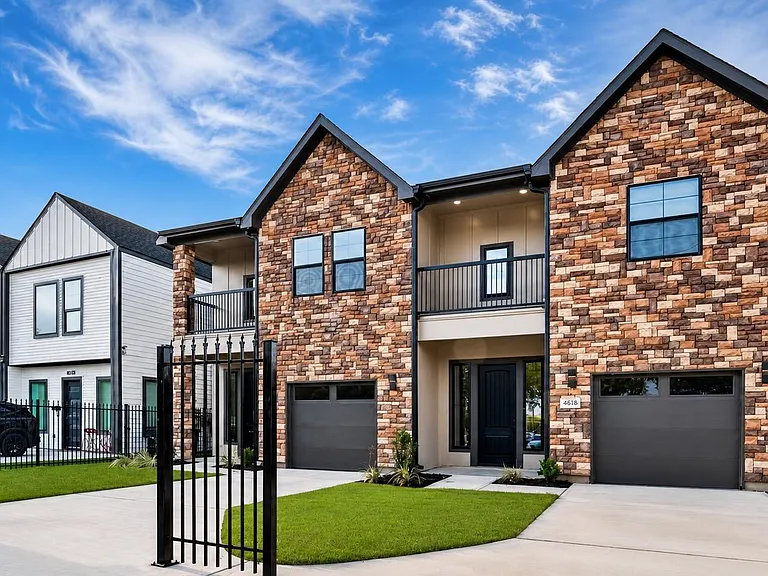 Well-kept two-story home with stone exterior, private driveway and garages, plus a small balcony and fenced front entry.