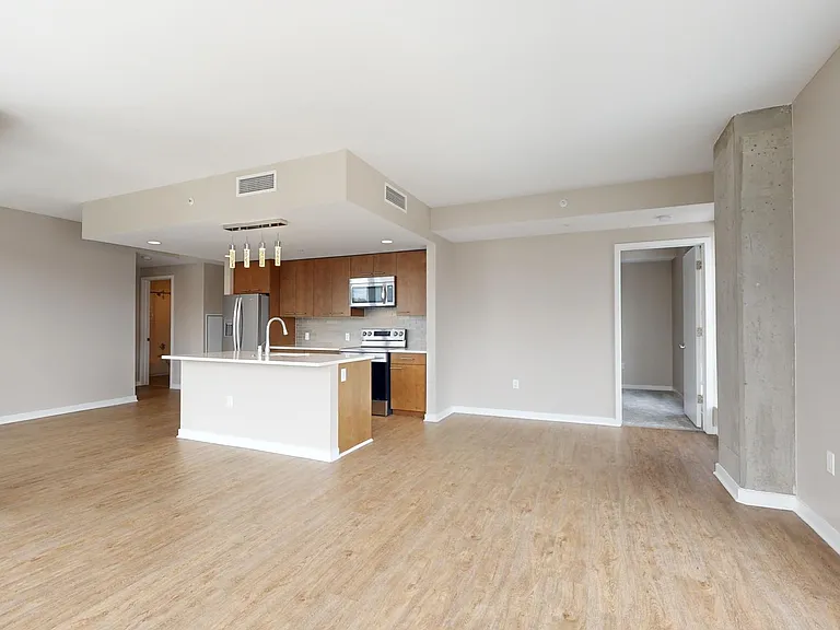 Apartment kitchen with stainless steel appliances, dining and living room with wood-style flooring.