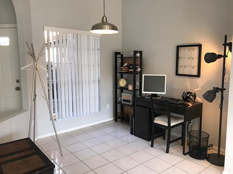 Entry area with tiled floors, a built-in front window and vertical blinds, plus a compact workstation and shelving.