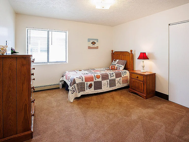 Charming bedroom featuring warm wooden furniture, cozy twin bed with colorful sports-themed quilt, and bright natural lighting.