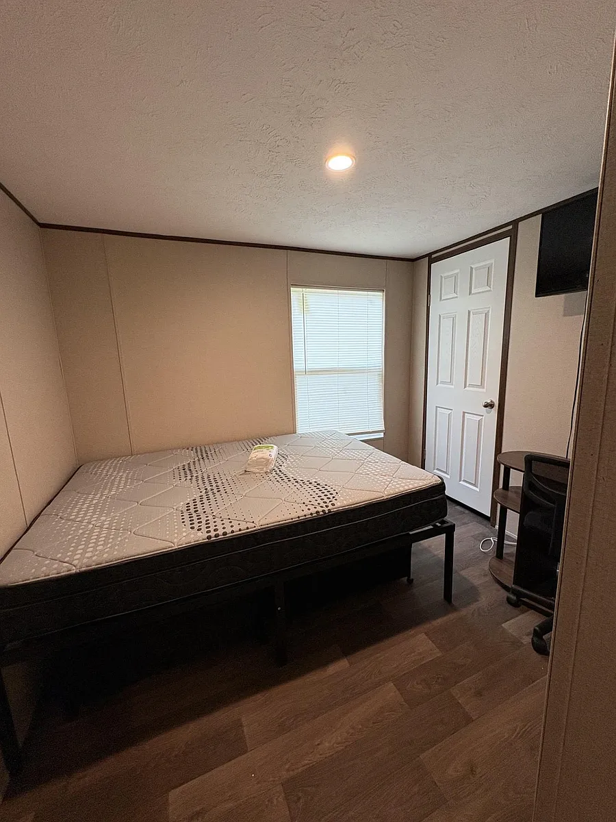 Private bedroom with wood-look flooring, a window with blinds, and space for a bed plus a small work area. - Eastern Ave