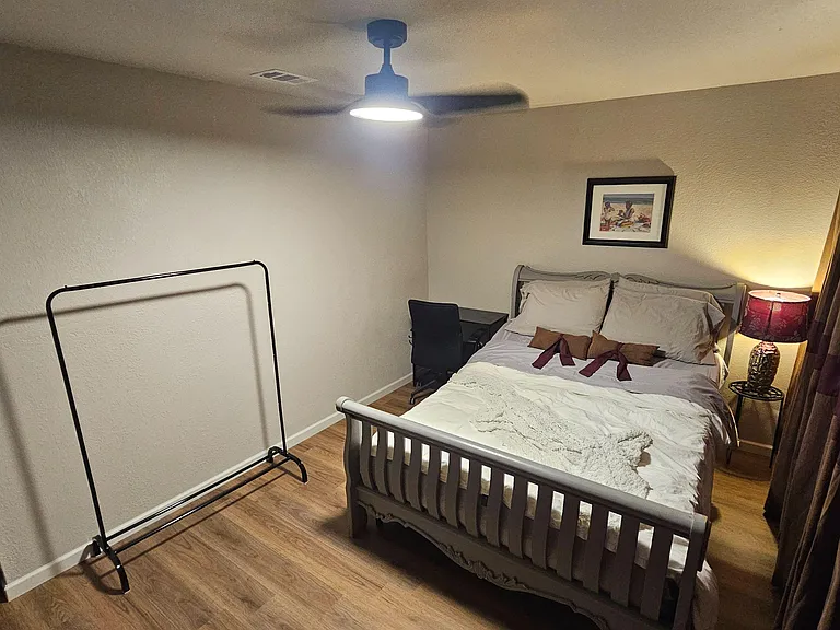 Furnished bedroom featuring a full bed, ceiling fan, bedside lighting, and space for a desk or clothing rack.