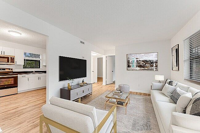 Modern open-concept living room with elegant furniture, wall art, and natural light flowing from large windows, seamlessly connected to a sleek kitchen.
