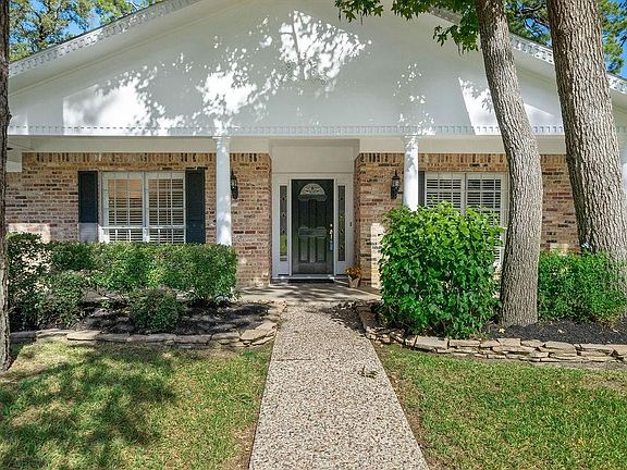 A closer look at the architectural columns and beautiful front door with glass side panels. Stone work surrounding the landscaped shrubs and mature trees.