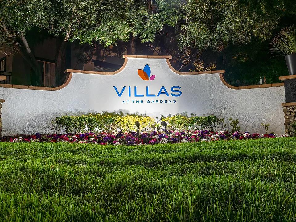 Villas at the Gardens Illuminated Entry Sign with Lush Lawn and Colorful Flowers