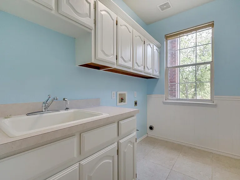 Laundry room featuring a utility sink, white cabinetry, and a window