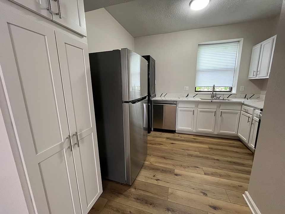 Kitchen long view. In the front, 7-foot-high soft-close cabinet pantry. A stainless steel refrigerator is behind it.