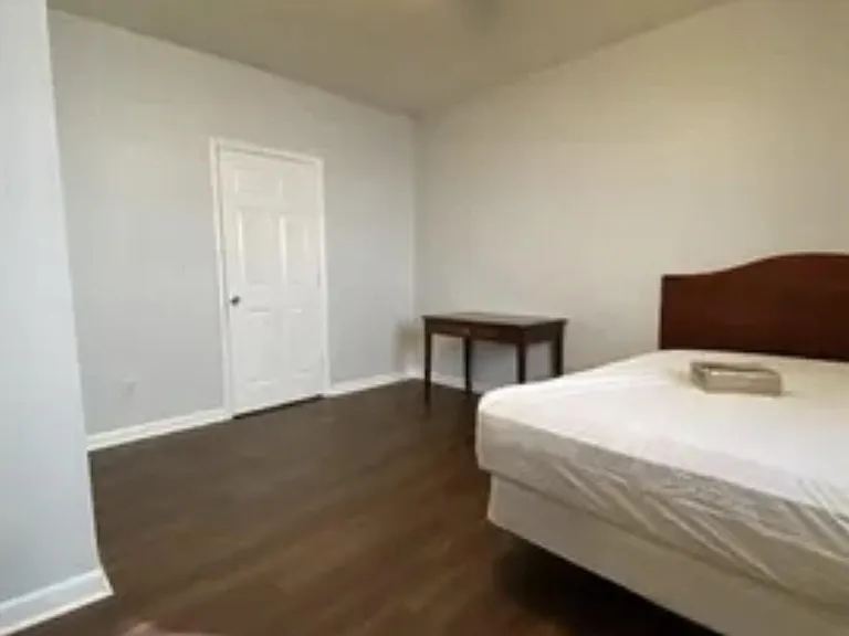 Private bedroom with hardwood-style flooring, ceiling fan with light, and space for a bed plus a small work table.