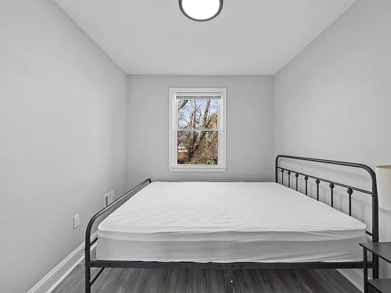 Private bedroom with a metal bed frame, neutral walls, and a window with blinds for natural light and ventilation.
