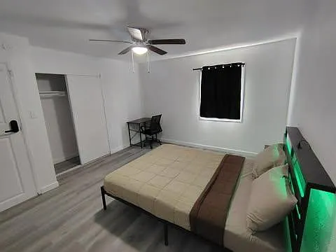 Spacious bedroom with a ceiling fan, bed setup, dedicated desk area, and a closet for convenient storage.