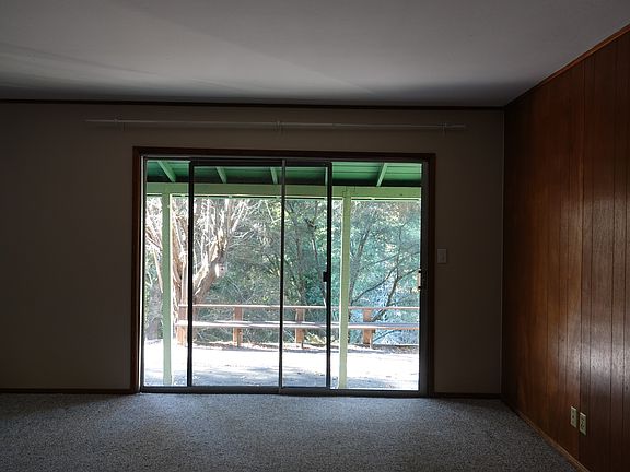 Spacious living room with original wood paneling and large sliding glass doors opening to a covered patio and wooded views.