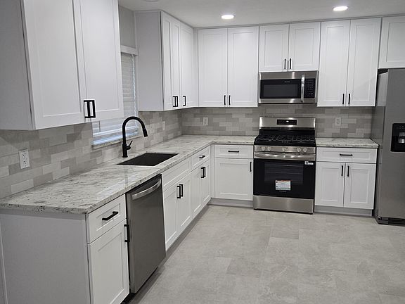 Beautifully remodeled kitchen featuring white shaker cabinets, granite counter tops, stainless steel appliances, and modern black accents.