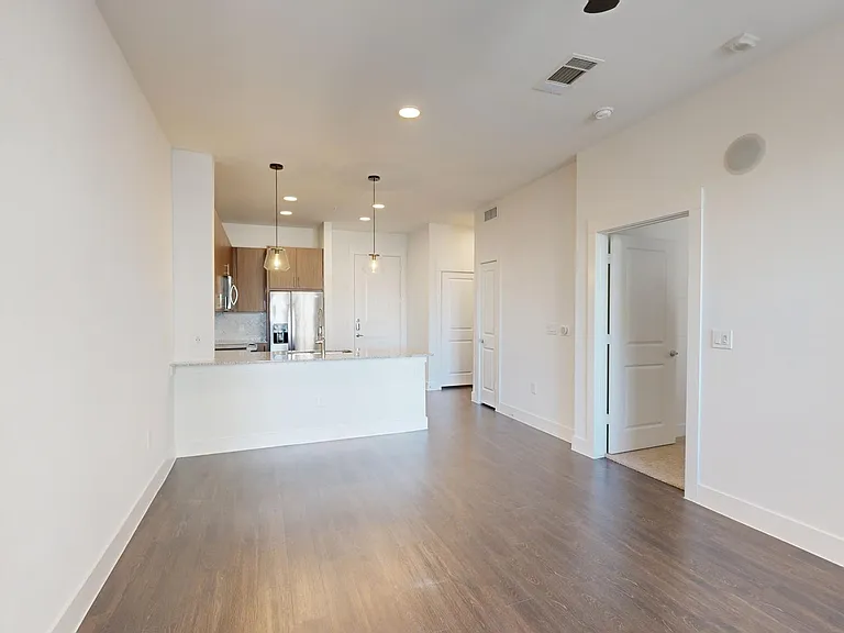 Apartment kitchen with stainless steel appliances, dining and living room with wood-style flooring.