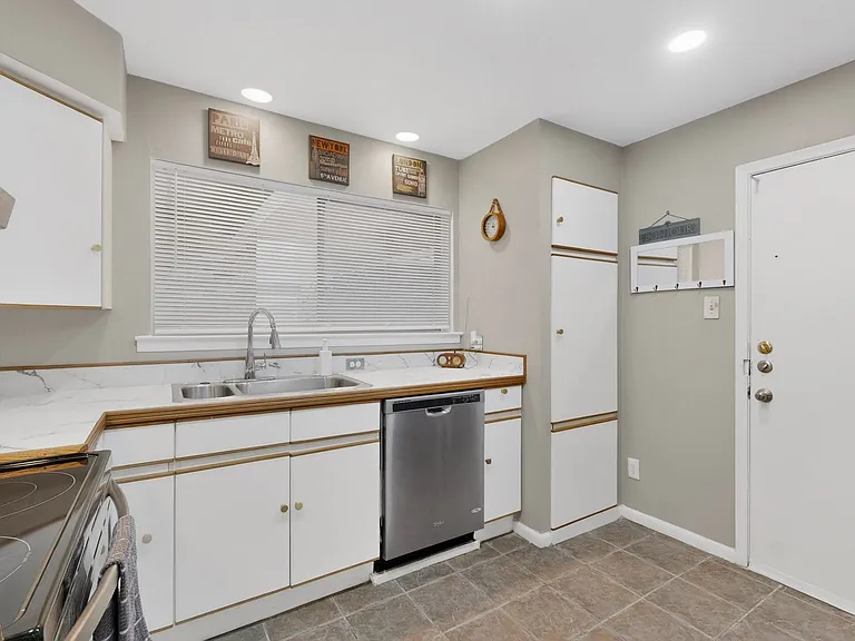 Bright kitchen with white cabinetry, dual sink, a wide window and sleek stainless steel appliances.