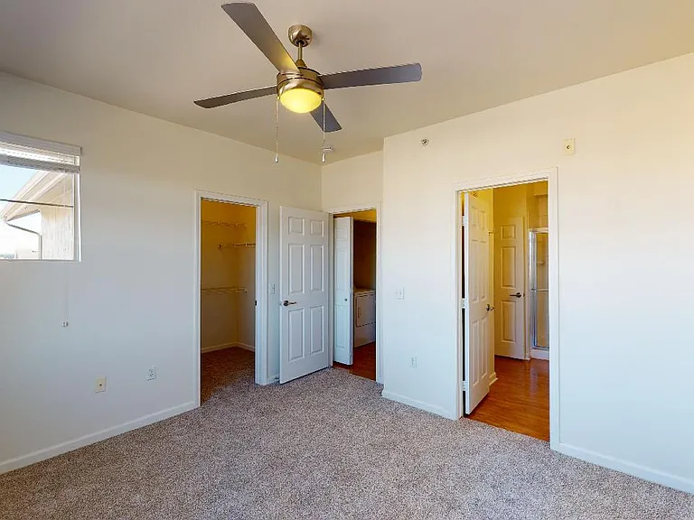 Spacious apartment bedroom with large closet, attached bathroom and plush carpet flooring.