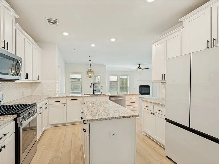 Kitchen featuring white shaker cabinetry, light-toned granite countertops, stainless steel appliances, a center island, and wood-finish flooring