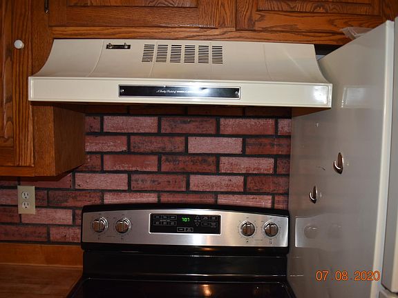 Stove with hood next to refrigerator and oak cabinets