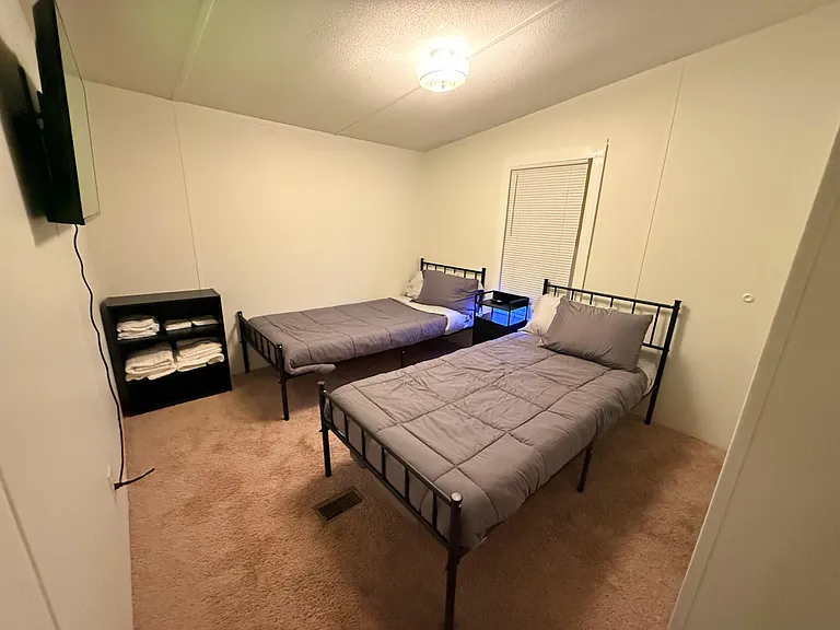 Furnished shared bedroom with two twin beds, a nightstand, and shelving, plus a window with blinds for privacy.