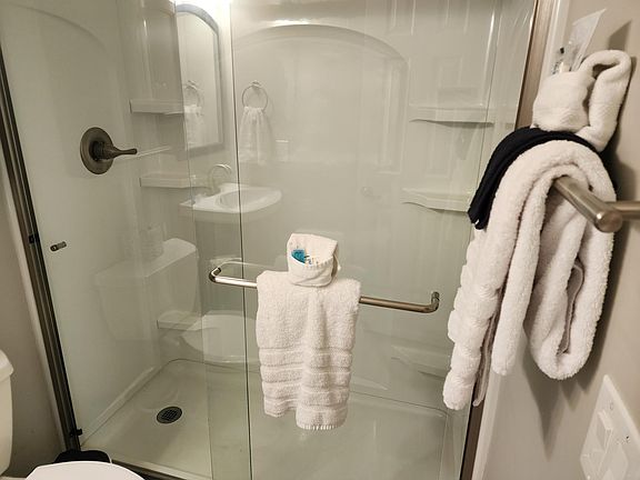 Glass shower door for this primary ensuite bathroom, bathroom offers extra cabinetry over the toilet, and under the sink. Shower has plenty of space to store soaps, etc.