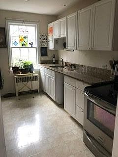 The bright renovated kitchen has granite countertop, white cabinets, electric stove, and pantry.