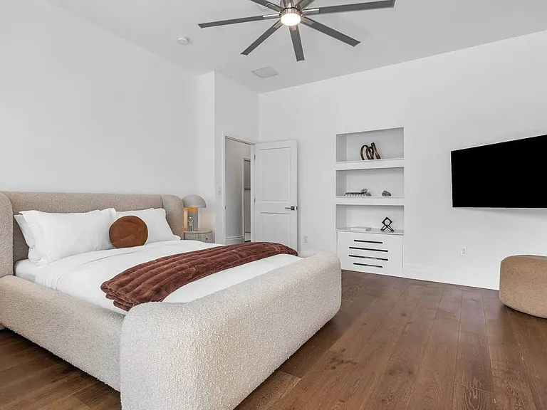 Sink into comfort in the stylish guest bedroom, featuring soft textures, warm wood floors, and built-in shelving.