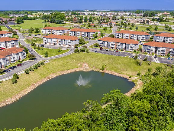 Explore the expansive grounds of Lenox West from above, featuring charming buildings, well-maintained landscapes, and a picturesque pond with a fountain.