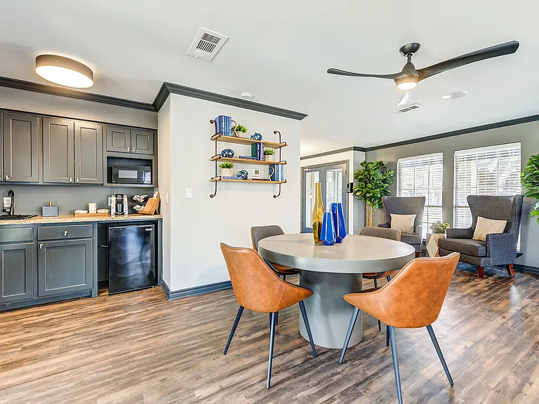 A leasing office table with orange chairs is shown next to a mini fridge and coffee station.
