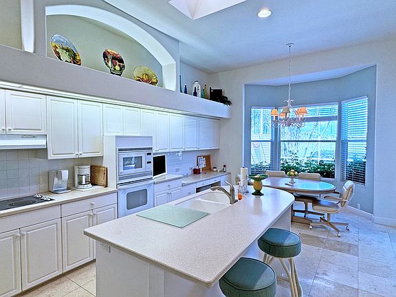 The large kitchen has tall ceilings with eating areas at the counter and a table facing the pool and golf course. It also has a desk area, left of the dining area.