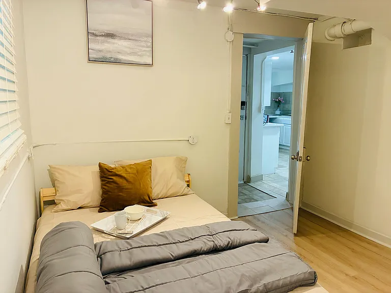 Furnished bedroom with a full-size bed, window blinds for light control, and convenient access to the nearby kitchen.