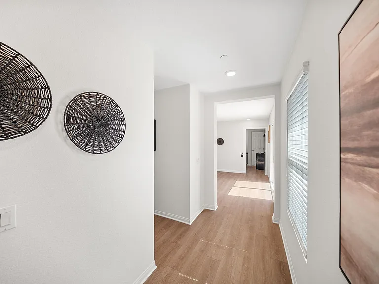 Wide hallway with wood-look flooring, recessed lighting, and a large window with blinds for natural light.