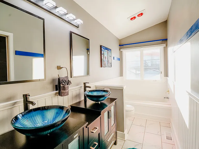 A bathroom featuring a unique blue sink, a wide mirror for an expansive feel, and a comfortable bathtub, blending functionality with serene aesthetics.