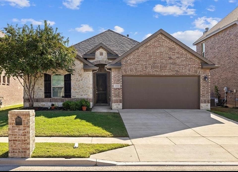 French country style house with brick siding, concrete driveway, a front yard, an attached garage, and roof with shingles