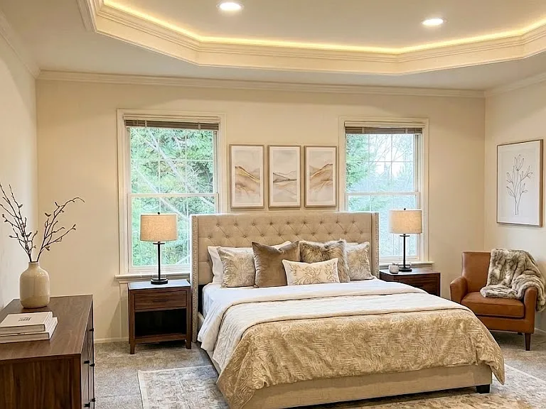 Expansive master retreat featuring elegant tray ceilings and large picture windows that frame serene, private tree-lined views (computer staged)