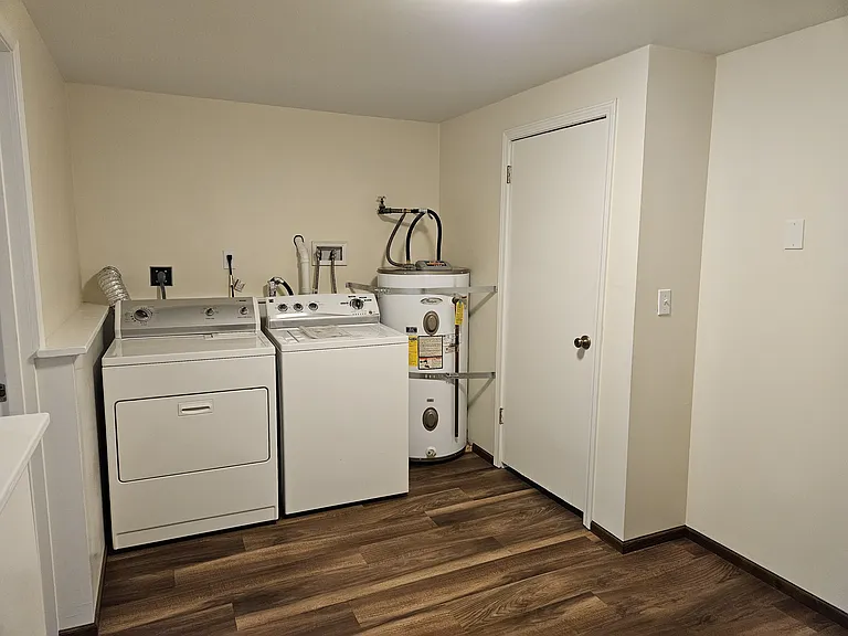 basement laundry room showing washing machine, dryer and hot water heater. laundry room is between bonus room and basement bedroom.