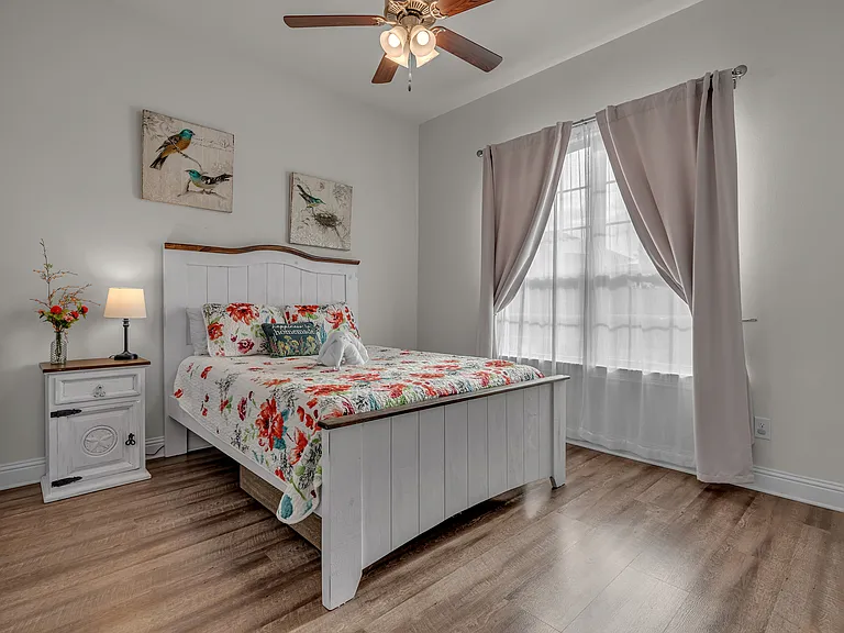 2nd guestroom in front of the home with a large closet, a queen bed, a pull-out drawer under, a side table, a lamp, and a ceiling fan.