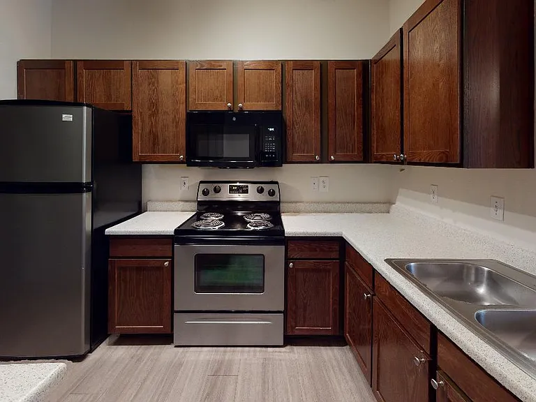 Apartment kitchen with stainless steel appliances, quartz countertops and wood-style flooring.