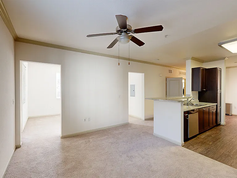 Apartment kitchen with stainless steel appliances, dining and living room with plush carpet flooring.