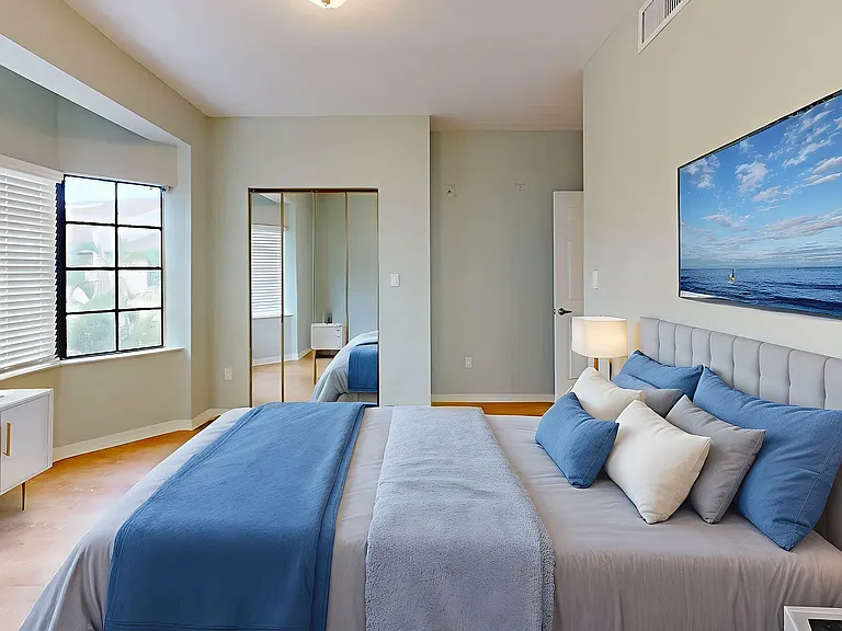 Elegant and spacious bedroom with stylish furnishings, large window with blinds, and a serene ocean artwork, illuminated by soft ambient lighting.