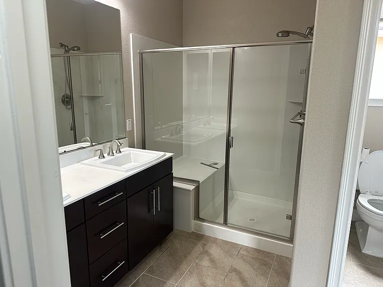 Luxurious primary bath with a spacious walk-in shower, sleek dark vanity, double sinks, and connected walk-in closet access.