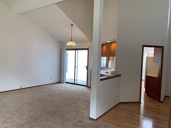 View from living room. Area under lowered light is a formal dining area. To the right of the formal dining area is the kitchen. Sliding glass doors open to a small patio. Wood flooring covers the entry area and the kitchen.