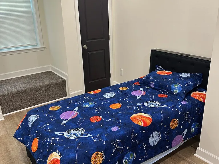 Furnished bedroom with a full bed, wood-look flooring, and a large window with blinds for privacy and natural light.